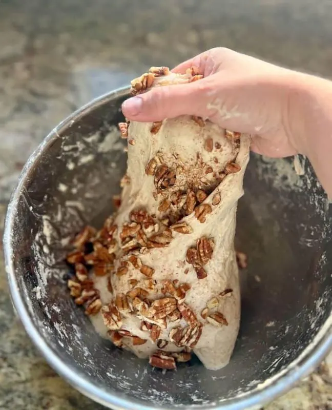Hands kneading bread dough with pecans in a bowl