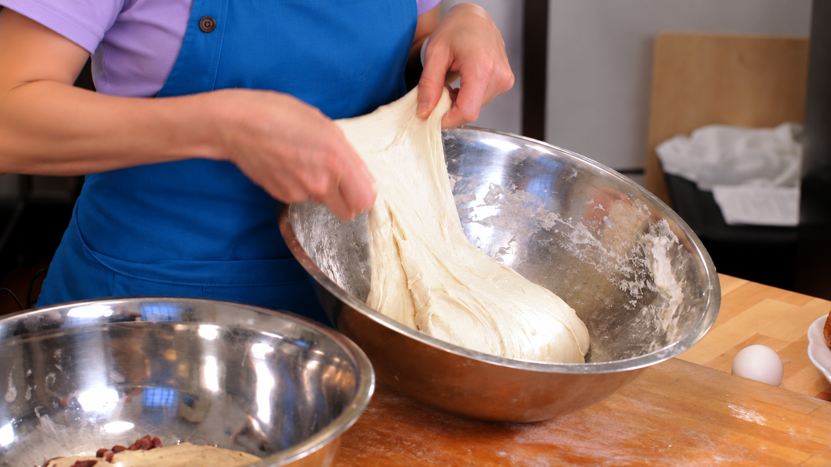 Hands stretching and folding bread dough in a steel bowl