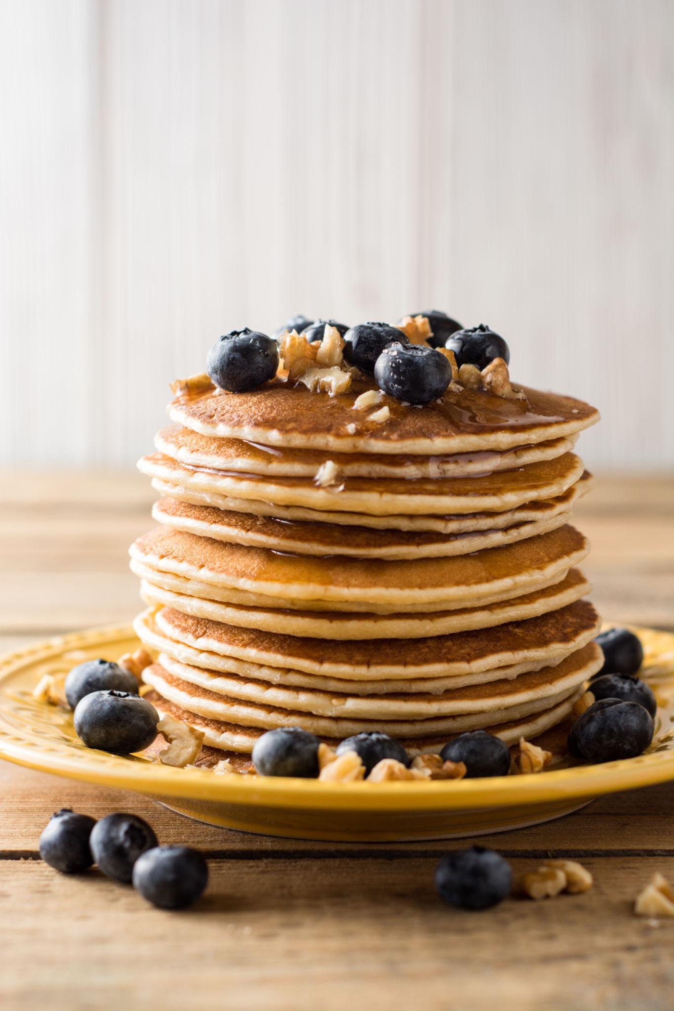 Stack of pancakes with blueberries and walnuts on a yellow plate