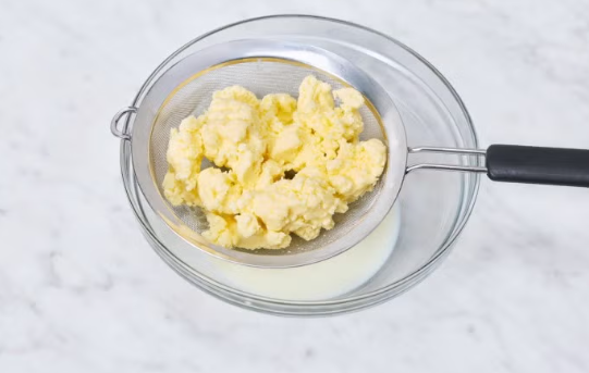 Freshly separated butter in a strainer over a bowl of buttermilk
