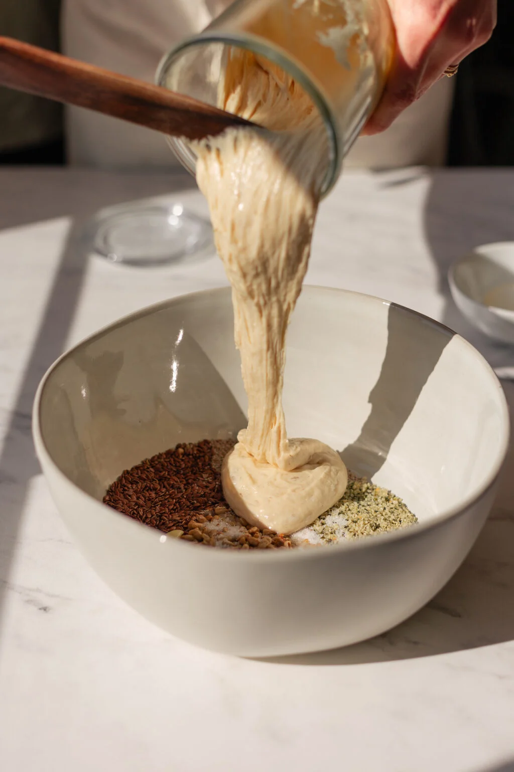 Sourdough starter being poured over seeds in a bowl